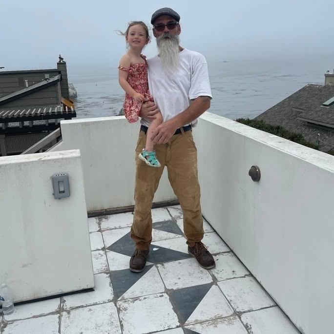 Robert Hedges, owner of The Tile Guys, holding a young girl on a tiled rooftop deck above the ocean