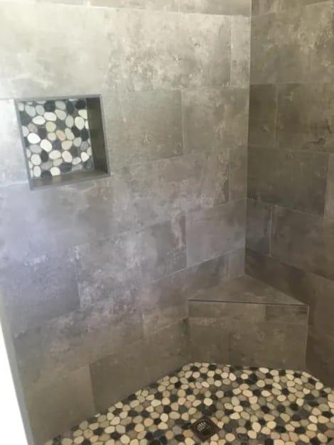 Gray tile shower wall with a pebble mosaic niche and a pebble floor.